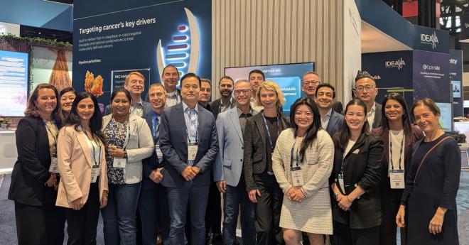 Group of people smiling, posing together at a conference or expo booth.